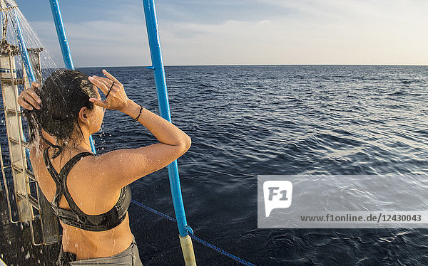 Rückansicht einer duschenden Frau auf einem im Meer segelnden Boot