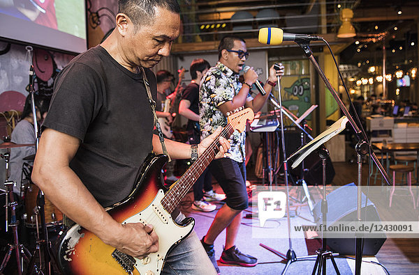 Asian band performing on stage with man playing electric guitar in foreground