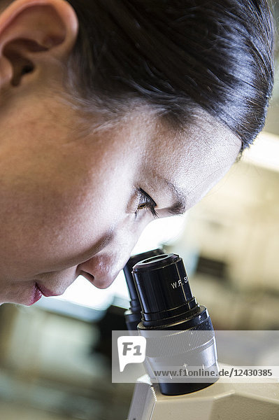A Caucasian female technician using a microscope to examine a part in a technical research and development site.