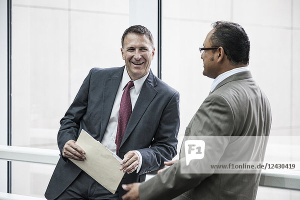 Two businessmen standing chatting in an open area of an office building.