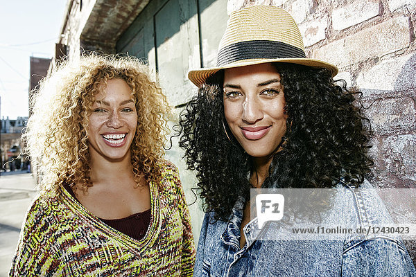 Portrait of two smiling young women with long curly black and blond hair  looking at camera.