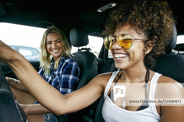 Portrait of two women with long blond and brown curly hair sitting in car  wearing sunglasses  smiling.