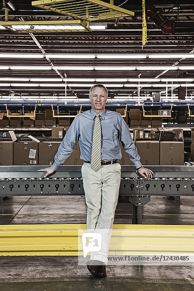Portrait of a male Caucasian executive in a dress shirt and tie next to a motorized conveyor system in a large distribution warehouse.
