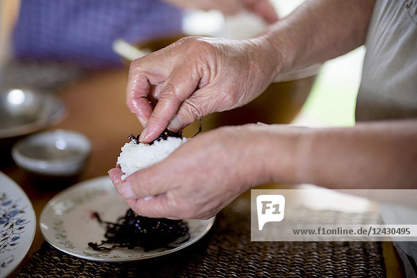 Nahaufnahme einer Frau  die in einer Küche an einem Tisch steht und Sushi zubereitet.
