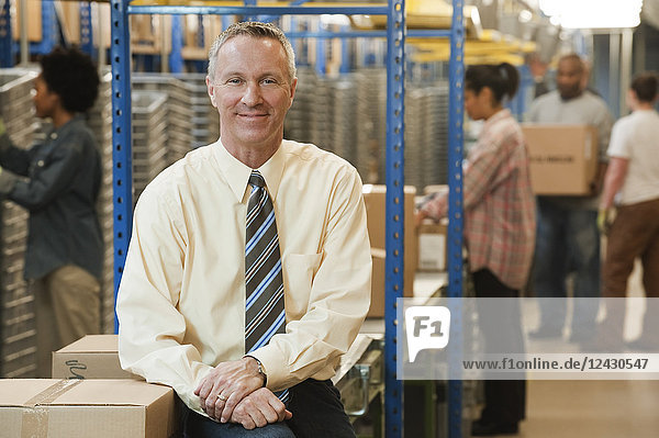 Portrait of a male Caucasian executive in a dress shirt and tie next to a motorized conveyor system in a large distribution warehouse.