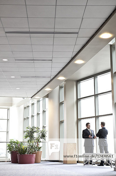 Two businessmen meeting in front of a window in a large convention centre lobby.