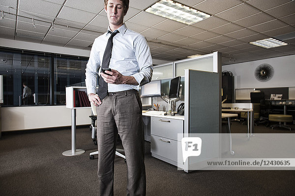 Caucasian businessman checking a text on his cell phone standing in his cubicle office.