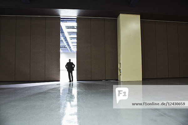 Businessman standing in a doorway between rooms in a convention centre arena.