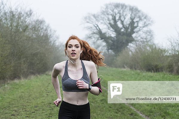 Young woman with long red hair wearing sports kit  exercising outdoors  looking at camera.