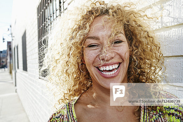 Portrait of young smiling woman with long curly blond hair  looking at camera.
