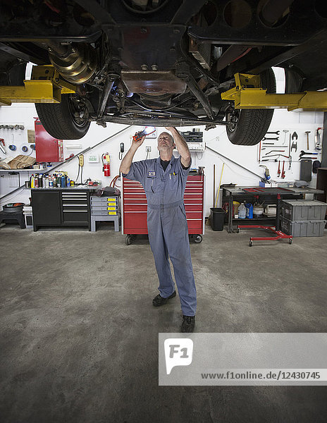Ein kaukasischer männlicher Mechaniker  der in der Werkstatt an der Unterseite eines Autos arbeitet.