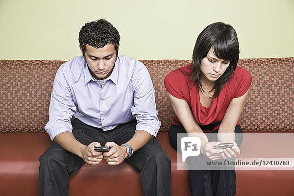 Ein spanischer Mann und eine kaukasische Frau mit je einem Mobiltelefon in einem Büro.