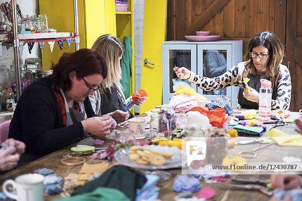 Gruppe von Frauen  die in einem Workshop um einen Tisch sitzen und Stoffblumen herstellen.