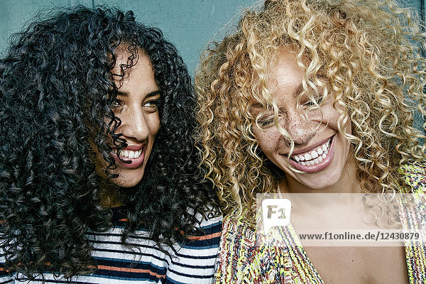 Porträt zweier junger Frauen mit langen lockigen schwarzen und blonden Haaren  lächelnd und lachend.
