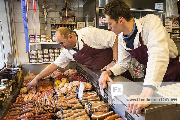 Two men wearing aprons standing at the counter of a butcher shop.