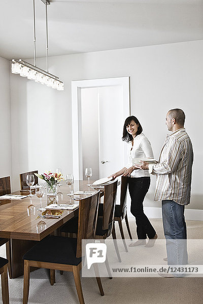 Hispanic man and woman doing place settings at their dinning room table in a new home.