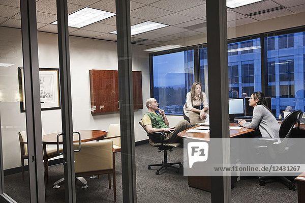 Blick durch die Tür von drei Personen  die in einem Büro an einem Projekt arbeiten.