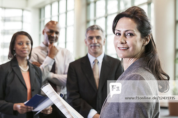 A mixed race group portrait of business people standing in a convention centre lobby  with a business woman as the lead.