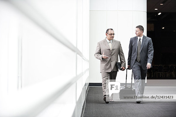An Hispanic businessman and a Caucasian businessman walking and talking together in a convention centre lobby