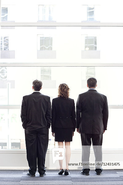 Rückansicht einer Gruppe von drei Geschäftsleuten  die aus dem Fenster einer Lobby eines Konferenzzentrums blicken.