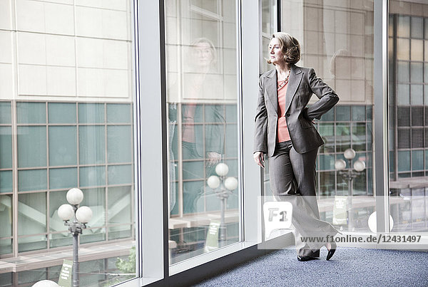 A Caucasian businesswoman standing next to a large window in a convention centre lobby.