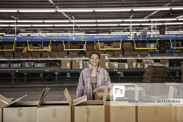 Porträt einer afroamerikanischen Lagerarbeiterin in einem großen Vertriebslager mit in Pappkartons gelagerten Produkten.