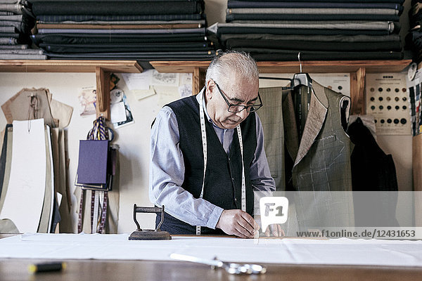 Tailor with measuring tape around neck working with material at bench