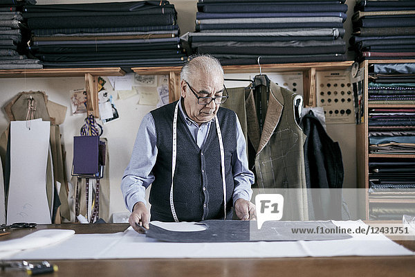 Tailor with measuring tape around neck working on a cut piece of fabric.