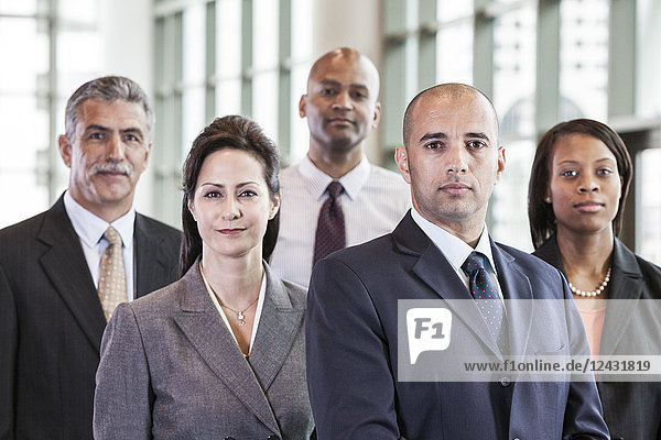 A mixed race group portrait of business people standing in a convention centre lobby.
