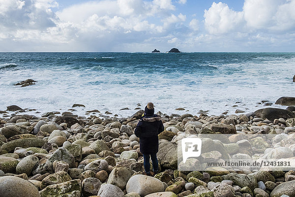 Eine Frau steht auf den Felsen und blickt auf die Küste von Cornwall und die brechenden Wellen.