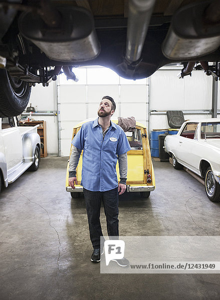 Ein Automechaniker  der in einer Werkstatt das Fahrgestell eines Autos überprüft  an dem er gerade arbeitet.