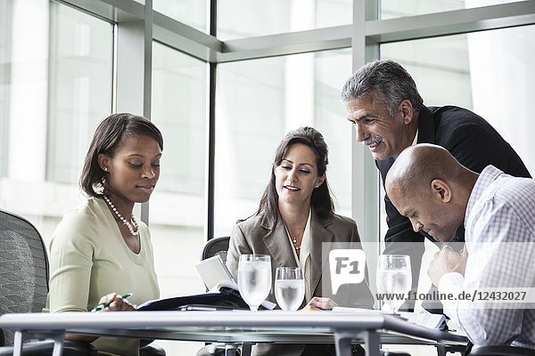 A mixed race group of male and female business people in a meeting at a conference table next to a large window in a convention centre.