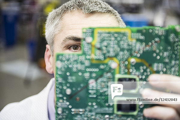 A Caucasian male technician examining a circuit board in a technical research and development site.