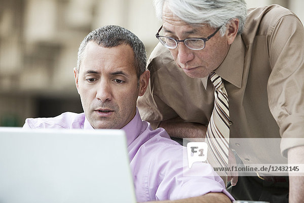 Ein asiatischer Geschäftsmann und ein kaukasischer Geschäftsmann arbeiten an einem Lap-Top-Computer in der Lobby eines Kongresszentrums.