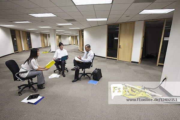 Eine gemischtrassige Gruppe von drei Geschäftsleuten  die in einem offenen Raum sitzen und Pläne für ein neues Bürolayout schmieden.