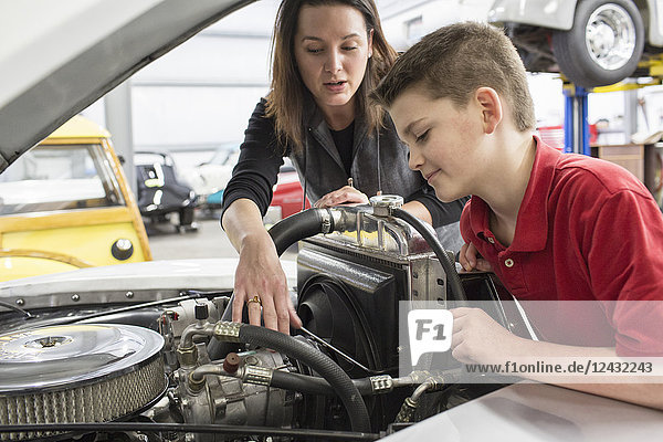 Eine kaukasische Automechanikerin spricht mit ihrem kleinen Sohn über einen Automotor in einer Oldtimer-Werkstatt.