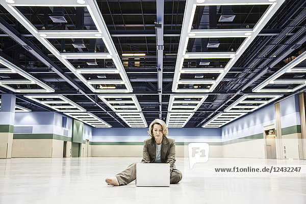 Eine kaukasische Geschäftsfrau arbeitet an einem Laptop-Computer  während sie auf dem Boden eines Kongresszentrums sitzt.