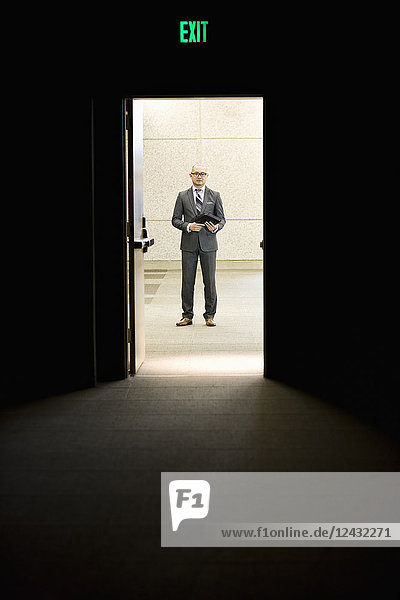 Businessman standing in a doorway between rooms in a convention centre arena.