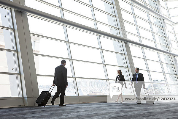 Three business people walking next to a large window in a conference centre lobby.