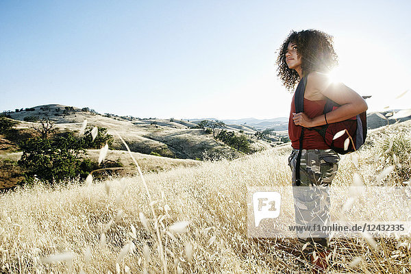 Young woman with curly brown hair hiking in urban park.