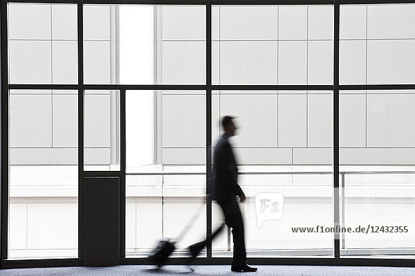 A businessman blurred in silhouette while walking past a large window in a convention centre lobby.