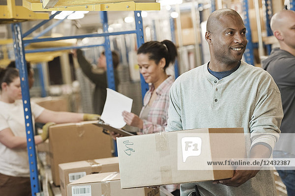 African American warehouse worker and a team of multi-ethnic workers working next to a motorized conveyor of cardboard boxes holding products in a large distribution warehouse.