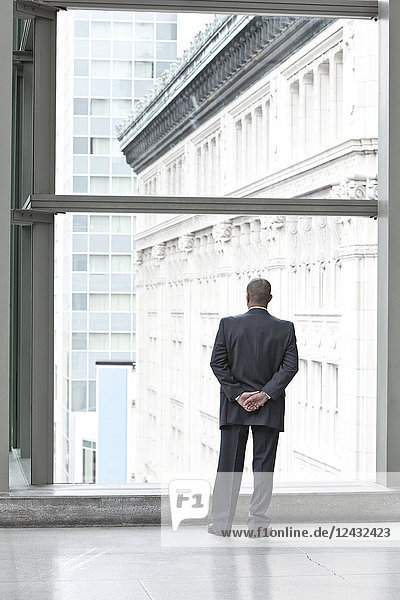 Ein Geschäftsmann steht am Fenster eines Kongresszentrums und blickt aus dem Fenster auf die Stadt im Hintergrund.