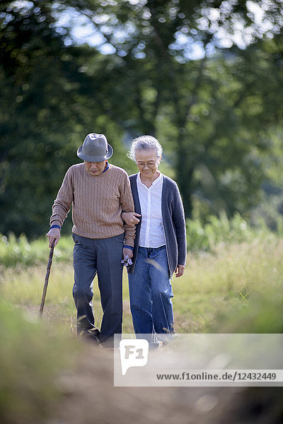 Husband and wife  elderly man wearing hat and using walking stick and elderly woman walking along path.