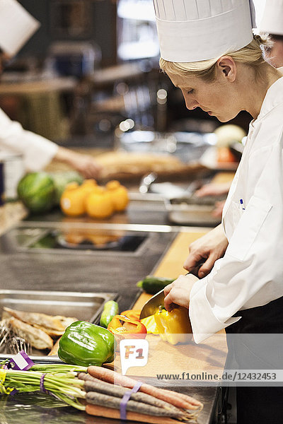 A Caucasian female chef works cutting vegetables in a commercial kitchen