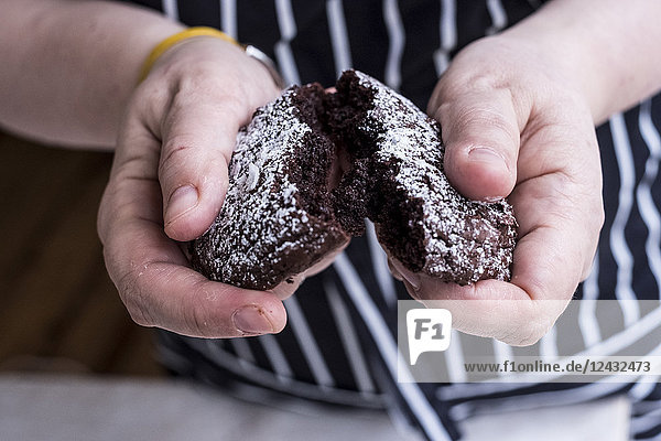 Ein Koch in einer Schürze  der einen in zwei Hälften gebrochenen Brownie-Kuchen aus dunkler Schokolade hält