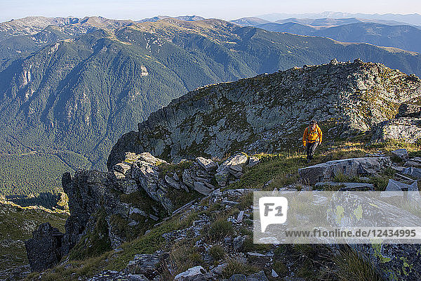 A hiker climbs along a high ridge near Maliovitsa in the Rila Mountains with distant views of valleys and hills Bulgaria Europe