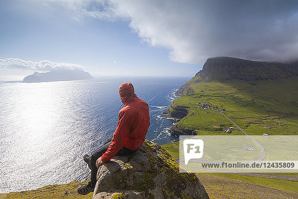 Hiker sitting on rocks looking at the ocean  Gasadalur  Vagar Island  Faroe Islands  Denmark  Europe