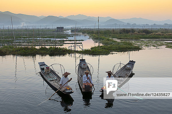 Three fishermen keep warm in their long tail fishing boats at dawn near the floating gardens on Inle Lake  Shan State  Myanmar (Burma)  Asia