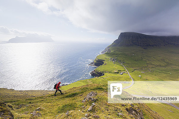 Hiker on steep hills towards Bour  Gasadalur  Vagar Island  Faroe Islands  Denmark  Europe